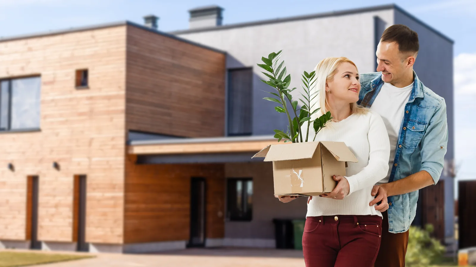 Un couple porte un carton devant sa maison neuve en bois